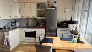 A compact kitchen with white cabinets, a stainless steel oven, a refrigerator, and a dining table with chairs. - 4 Star Holiday Home in Tranekaer (Tranekaer)