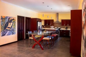 A modern kitchen with dark wooden cabinets, a glass dining table, and a large painting on the wall.