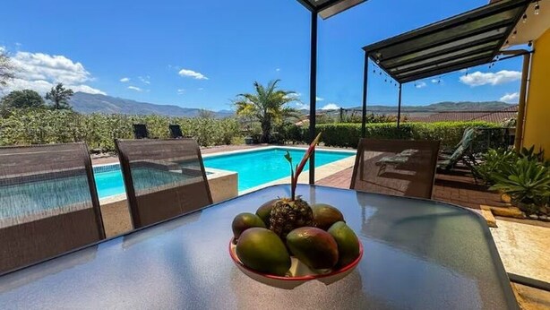 Ein Tisch am Pool mit einer Obstschale, ein Schwimmbecken und Blick auf Berge.
