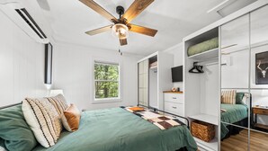 Une chambre à coucher avec un lit, un ventilateur de plafond, une fenêtre, une armoire et un miroir.