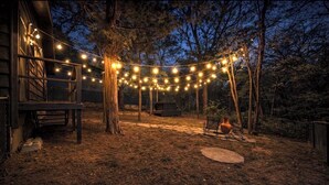 Un jardin avec des guirlandes lumineuses, une terrasse en bois et un coin salon extérieur de style rustique.