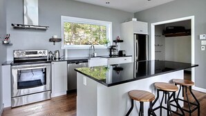 Een moderne keuken met een centraal eiland, roestvrijstalen apparatuur en een raam met uitzicht op groen.