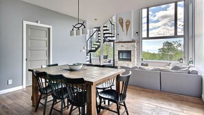 Een eethoek met een houten tafel en stoelen, een open haard en een groot raam met uitzicht.