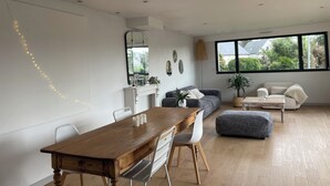 Un salon moderne comprenant un coin repas, une cheminée et une grande fenêtre donnant sur un paysage verdoyant.