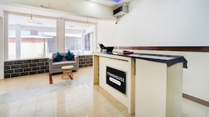 A reception desk with a sign reading 'TOWNHOUSE Company Services,' a sofa with blue cushions, a small round table, and a view through large windows. - Deluxe Keyen Arcade (Kanayannur)