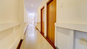 A long, narrow hallway with white walls and wooden doors, each marked with a number. - Deluxe Keyen Arcade (Kanayannur)