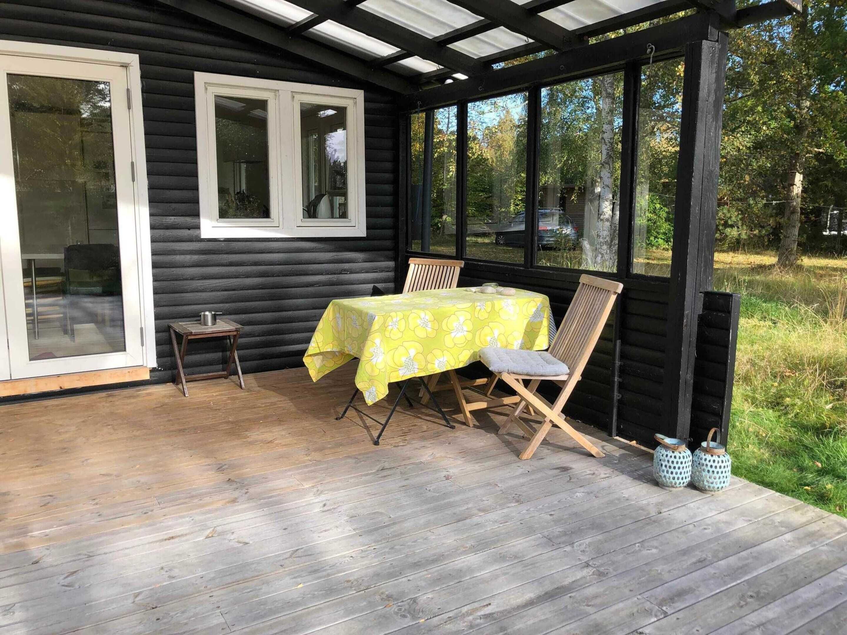 Ett trädäck med ett bord och stolar, ett takförsett område med fönster och en dörr.