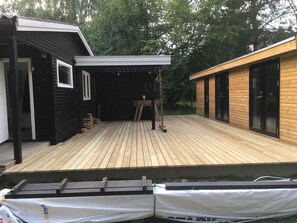 Eine Holzterrasse mit überdachtem Bereich, einem kleinen Tisch und einer Bank.