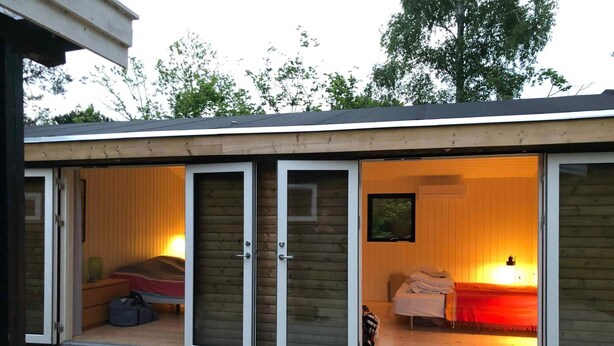 A single-room cabin with a sliding door, a bed, a small table, and a window. - 4 Star Holiday Home in Nykobing Sj (Nykobing Sjaelland)