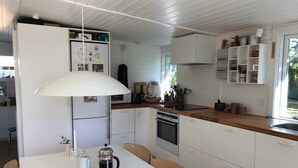 A modern kitchen with white cabinets, a coffee maker, and a dining table with chairs. - 4 Star Holiday Home in Nykobing Sj (Nykobing Sjaelland)