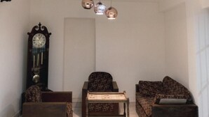 A living room with a sofa, armchair, small table, and a wall-mounted clock. - Mavick Gardens Apartment for rent per day (Anuradhapura)