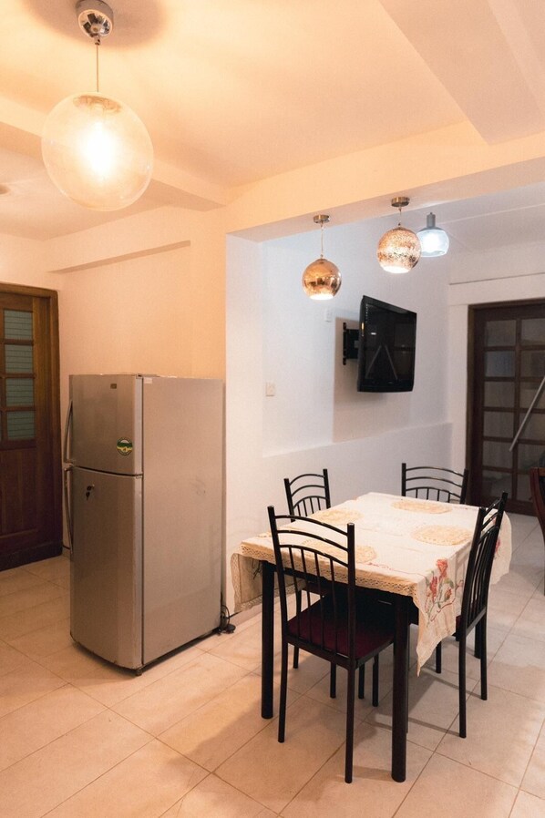 A dining area with a table, chairs, a refrigerator, and pendant lights.
