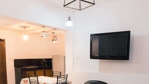 A living room with a dining area, a black leather chair, a small table, and a TV mounted on the wall. - Mavick Gardens Apartment for rent per day (Anuradhapura)