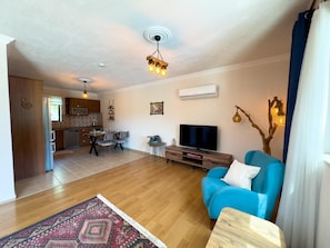 A living room with a blue sofa, a TV, a wooden coffee table, a patterned rug, and a kitchen in the background. - Villa Casa de Piedra (Fethiye)