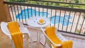 Ein Balkon mit zwei weißen Stühlen und einem Tisch, einem Glas Wasser und einem Glas Orangensaft.