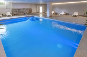 Ein Hallenbad mit klarem Wasser, einem Sprungturm und weißen Liegestühlen.