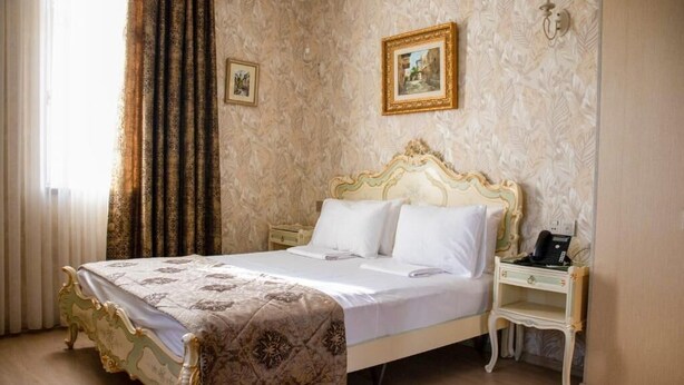 A classic four-poster bed with a white and gold frame, a bedside table with a telephone, and a wall with a floral wallpaper pattern. - Moon Light Hotel (Baku)