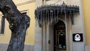 A building with a large tree in front, a decorative entrance, and a sign with a logo. - Moon Light Hotel (Baku)
