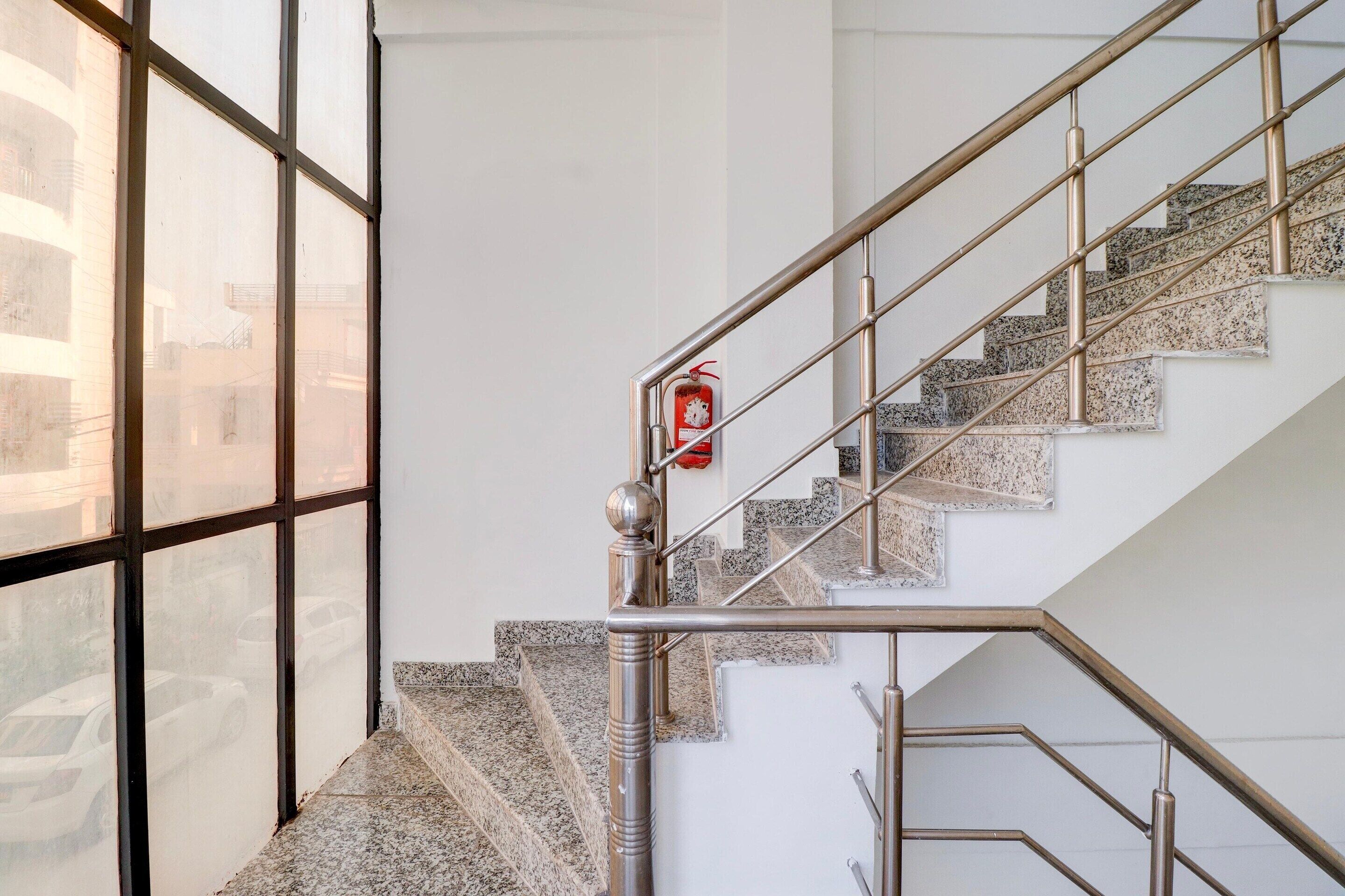 A staircase with metal railings and granite steps, a fire extinguisher mounted on the wall, and a large window on the left.