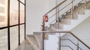 A staircase with metal railings and granite steps, a fire extinguisher mounted on the wall, and a large window on the left. - Deluxe Benison Guest House (Dehradun)