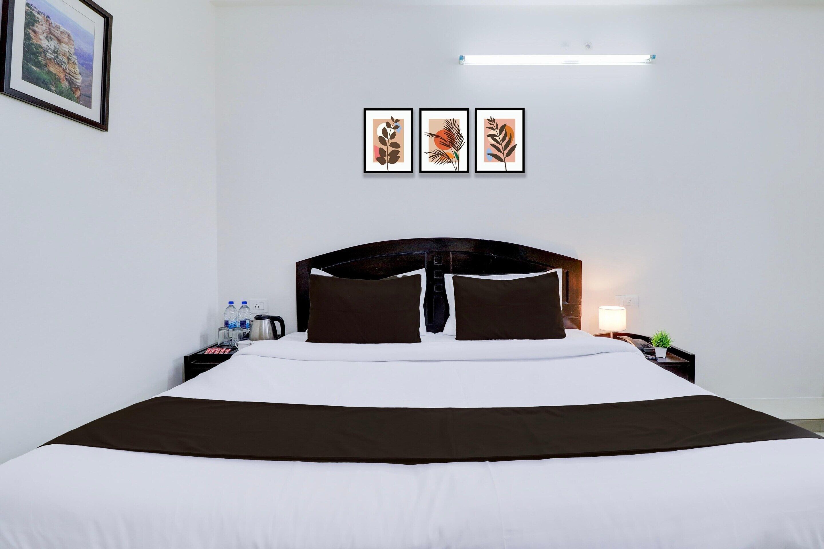 A hotel room with a large bed, a nightstand with a lamp, and three framed artworks on the wall.
