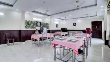 A dining area with tables set for service, a clock on the wall, and ceiling fans.