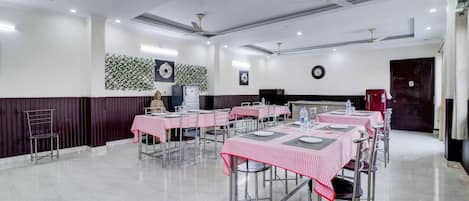 A dining area with tables set for service, a clock on the wall, and ceiling fans.