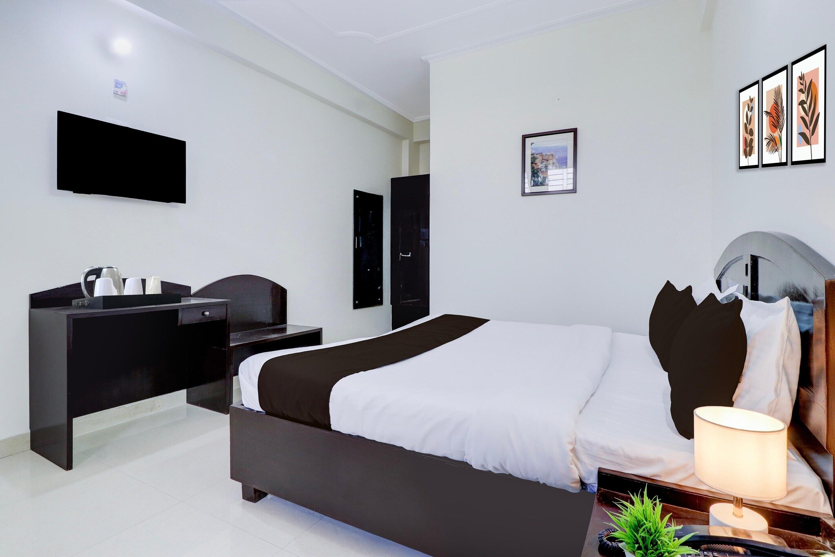 A hotel room with a bed, bedside table, lamp, and a flat-screen TV mounted on the wall.