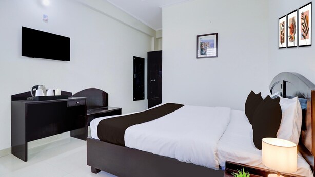 A hotel room with a bed, bedside table, lamp, and a flat-screen TV mounted on the wall. - Deluxe Benison Guest House (Dehradun)