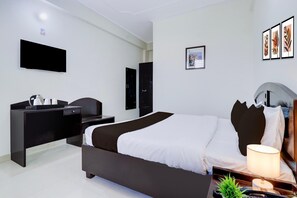 A hotel room with a bed, bedside table, lamp, and a flat-screen TV mounted on the wall. - Deluxe Benison Guest House (Dehradun)