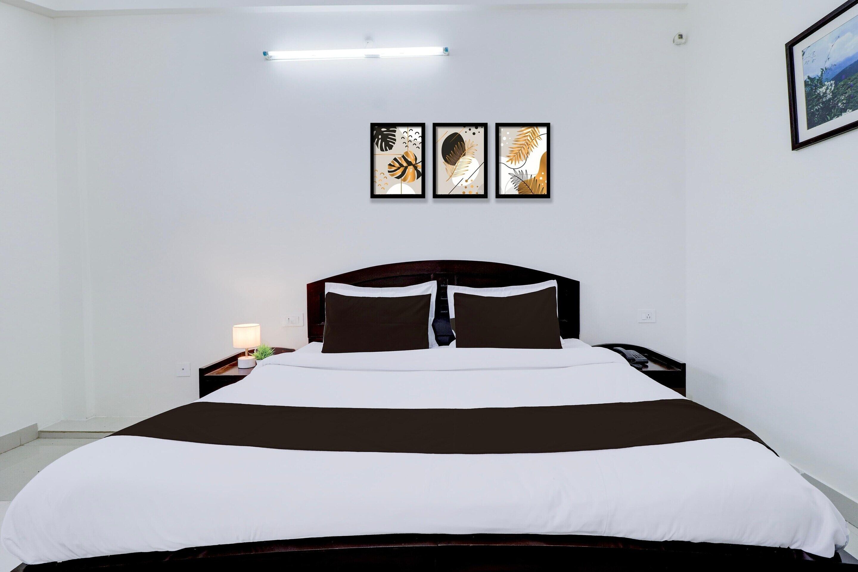 A hotel room with a bed, a nightstand, a lamp, and three framed artworks on the wall.