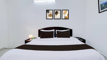 A hotel room with a bed, a nightstand, a lamp, and three framed artworks on the wall.