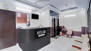 A hotel reception area with a reception desk, seating area, and a clock on the wall. - Deluxe Benison Guest House (Dehradun)