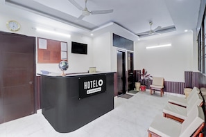 A hotel reception area with a reception desk, seating area, and a clock on the wall.