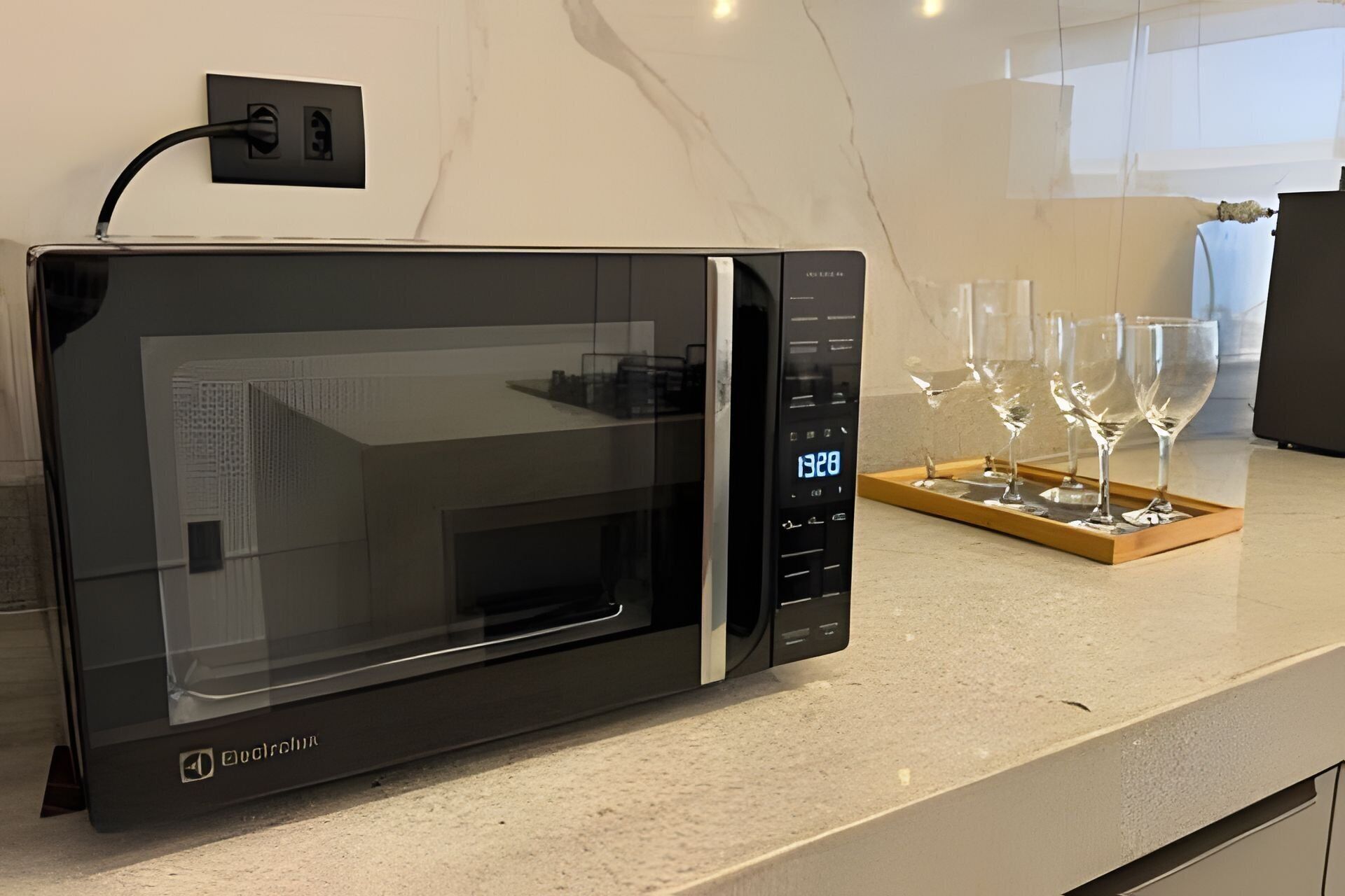 Een moderne keuken met een zwarte magnetron, een houten dienblad met wijnglazen en een marmeren aanrecht.