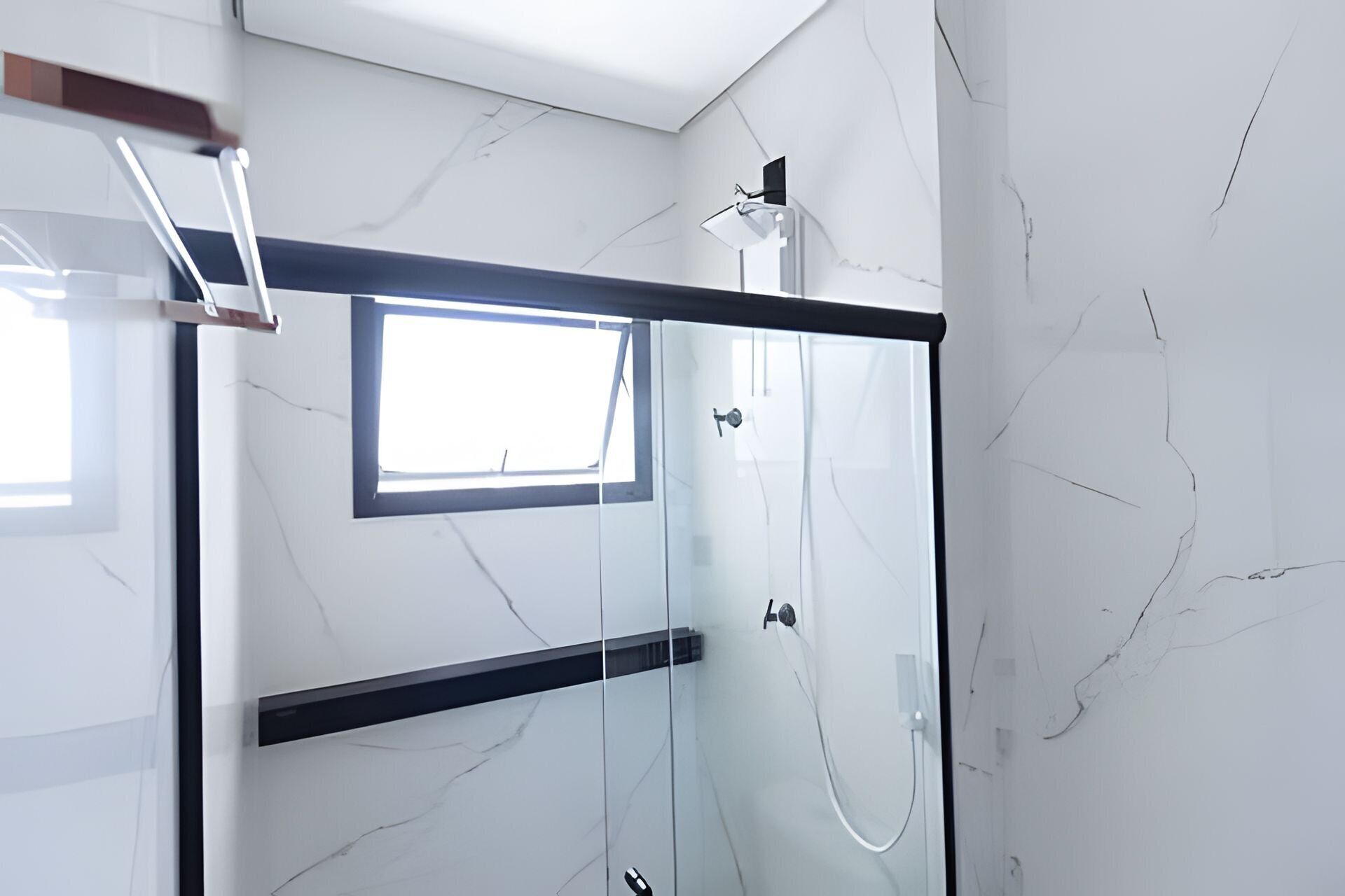 A modern bathroom with a glass shower enclosure, a small window, and a marble wall.