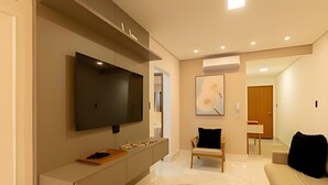 Ein modernes Wohnzimmer mit Flachbildfernseher, einer Couch, einem Couchtisch und einem gemusterten Teppich.