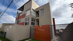 Un edificio moderno de varios pisos con techo plano, entrada protegida por una reja y un césped cuidado.