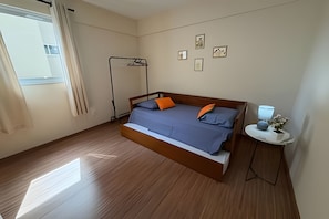 A bedroom with a bed, a bedside table with a lamp, a radiator, and a window with curtains.
