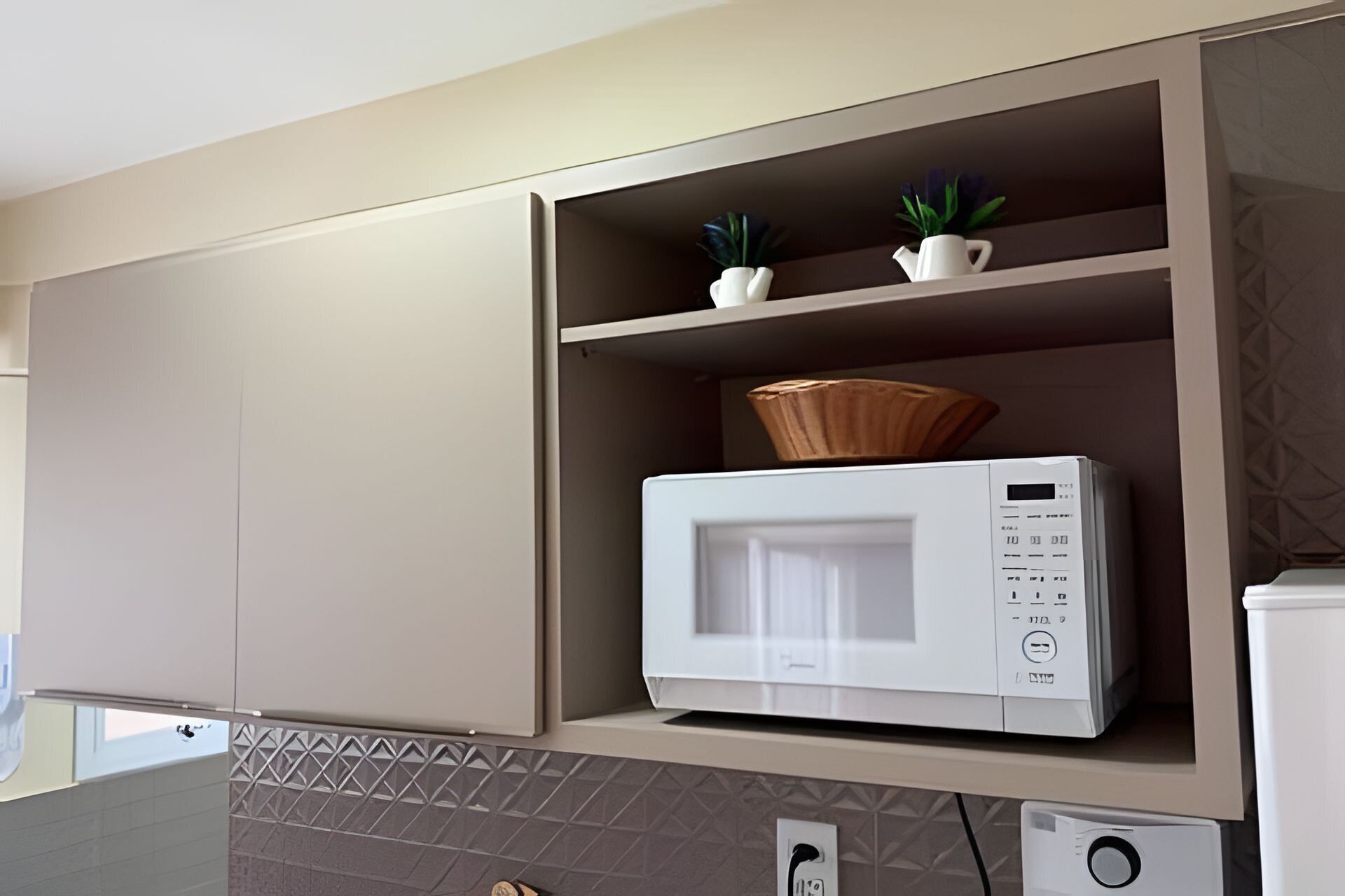 A kitchen with a microwave, a shelf with potted plants, and a patterned backsplash.