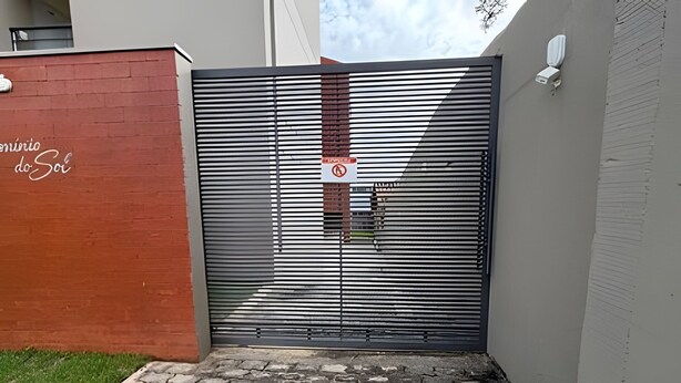 Una entrada cerrada con una barrera metálica, señal de prohibido pasar y un muro de ladrillo con grafitis.