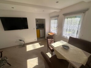 Ein Essbereich mit Tisch, Stühlen, einem an der Wand befestigten Fernseher und einer Küche im Hintergrund.