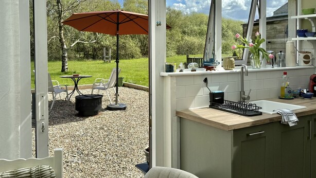 Una cucina con vista sulla finestra, un'area pranzo con sedie e un ombrellone, e un piccolo giardino esterno.