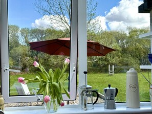A window with a view of a garden, a table with a coffee maker, and a vase with flowers. - Cottage 493 - Clifden - sleeps 5 guests  in 3 bedrooms (Clifden)