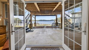 Un patio couvert avec vue sur un lac, des meubles d’extérieur et un escalier menant à un niveau supérieur.