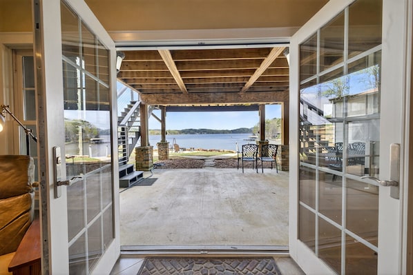 A covered patio with a view of a lake, outdoor furniture, and a staircase leading to an upper level.