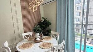A dining area with a round table, white chairs, woven placemats, and a hanging light fixture. - Apartment in Bávaro Punta Cana | Swimming Pool | Near the Beach (Punta Cana)