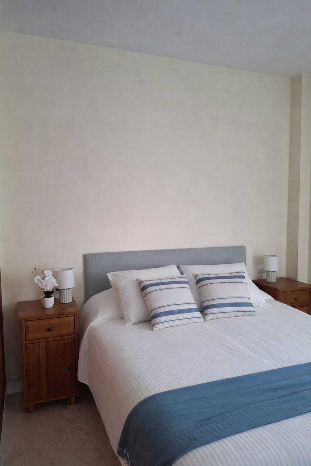 A bedroom with a bed, two bedside tables, a nightstand, a lamp, and a small potted plant.