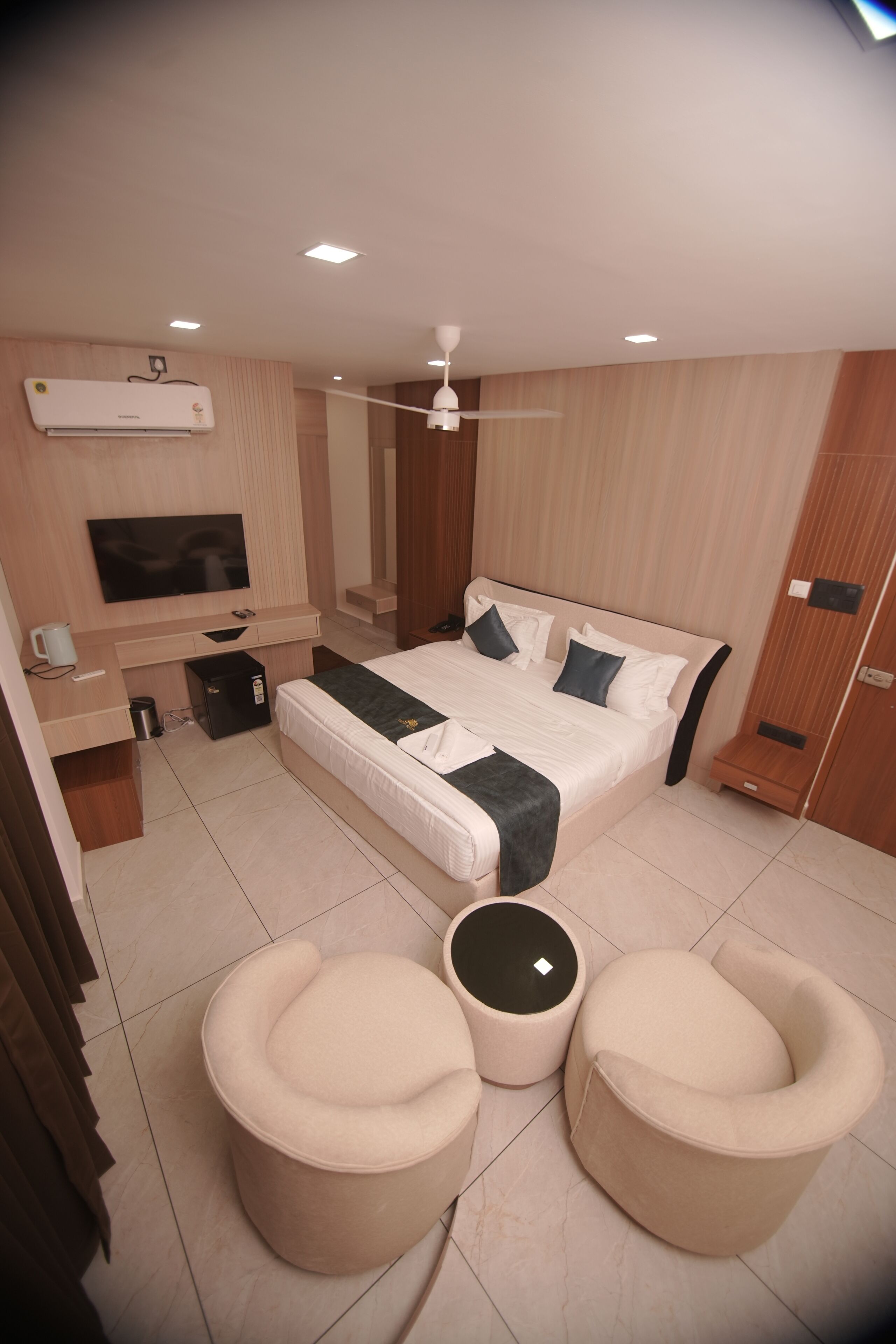 A modern hotel room with a large bed, a TV, a desk, and a seating area.