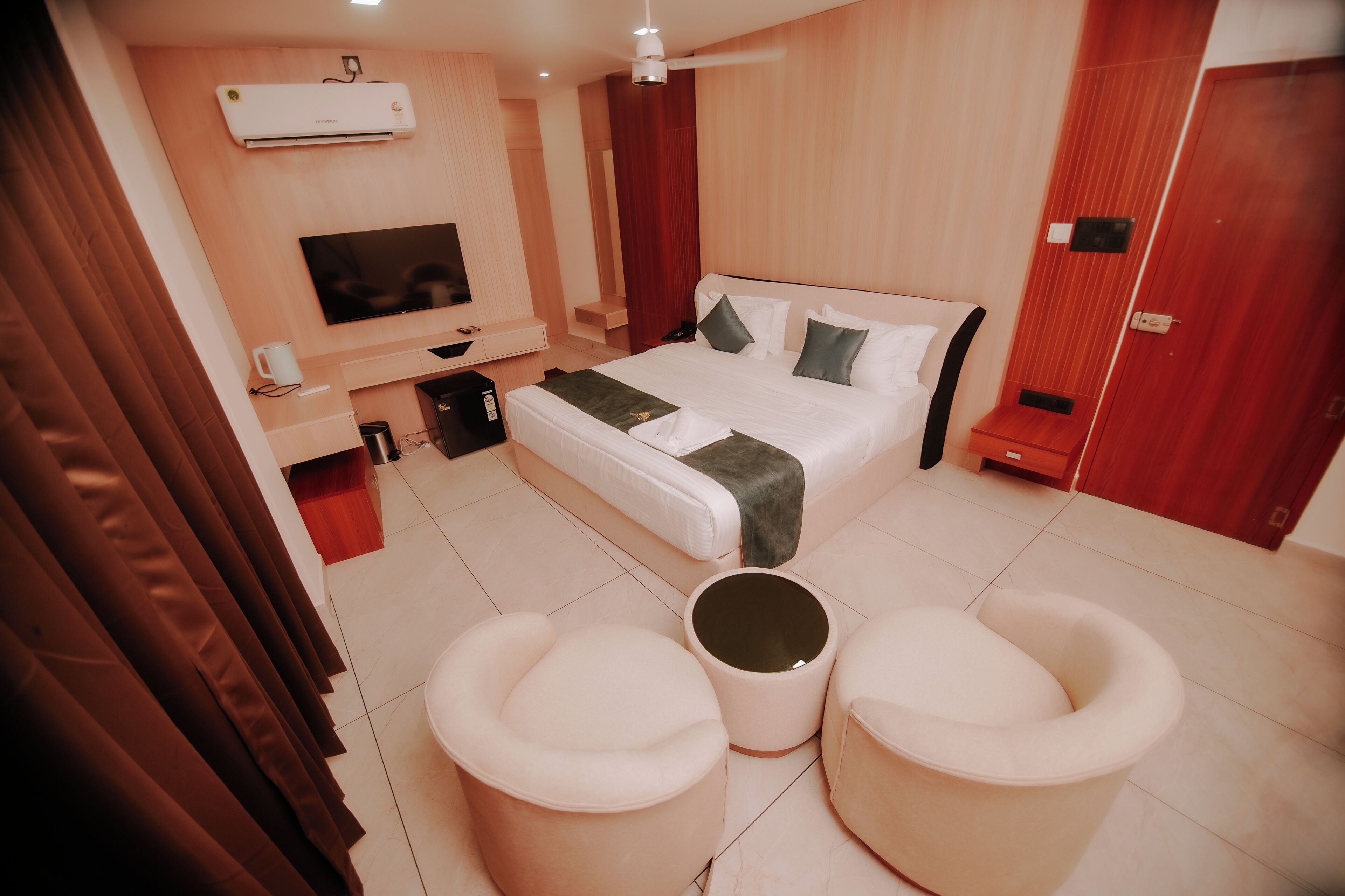Una habitación de hotel moderna con cama, televisor, cafetera y un área de descanso con dos taburetes.